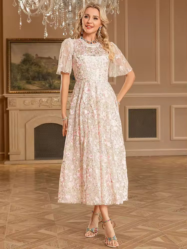 
                  
                    Woman in a floral dress standing in an elegant room with a chandelier and fireplace.
                  
                