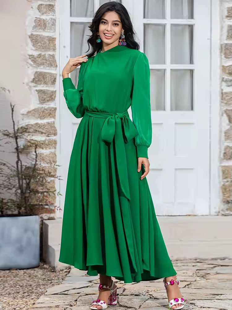 
                  
                    Woman wearing a green dress standing in front of a stone wall and white door.
                  
                