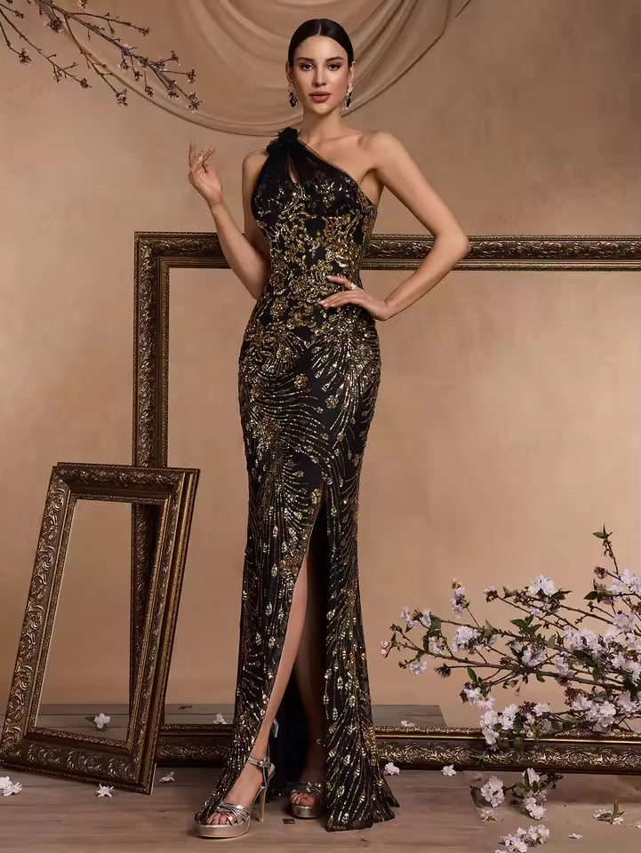 
                  
                    Woman in a black and gold evening gown standing in front of decorative frames and floral arrangements.
                  
                